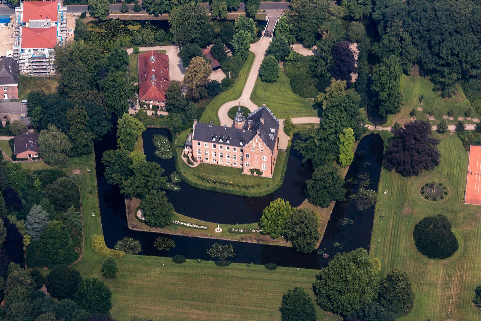 Luftaufnahme des Renaissance-Wasserschlosses Schloss Rhede mit seinen Backsteinflügeln, umgeben von Wassergraben und Bäumen – dem Wahrzeichen von Rhede im Kreis Borken.